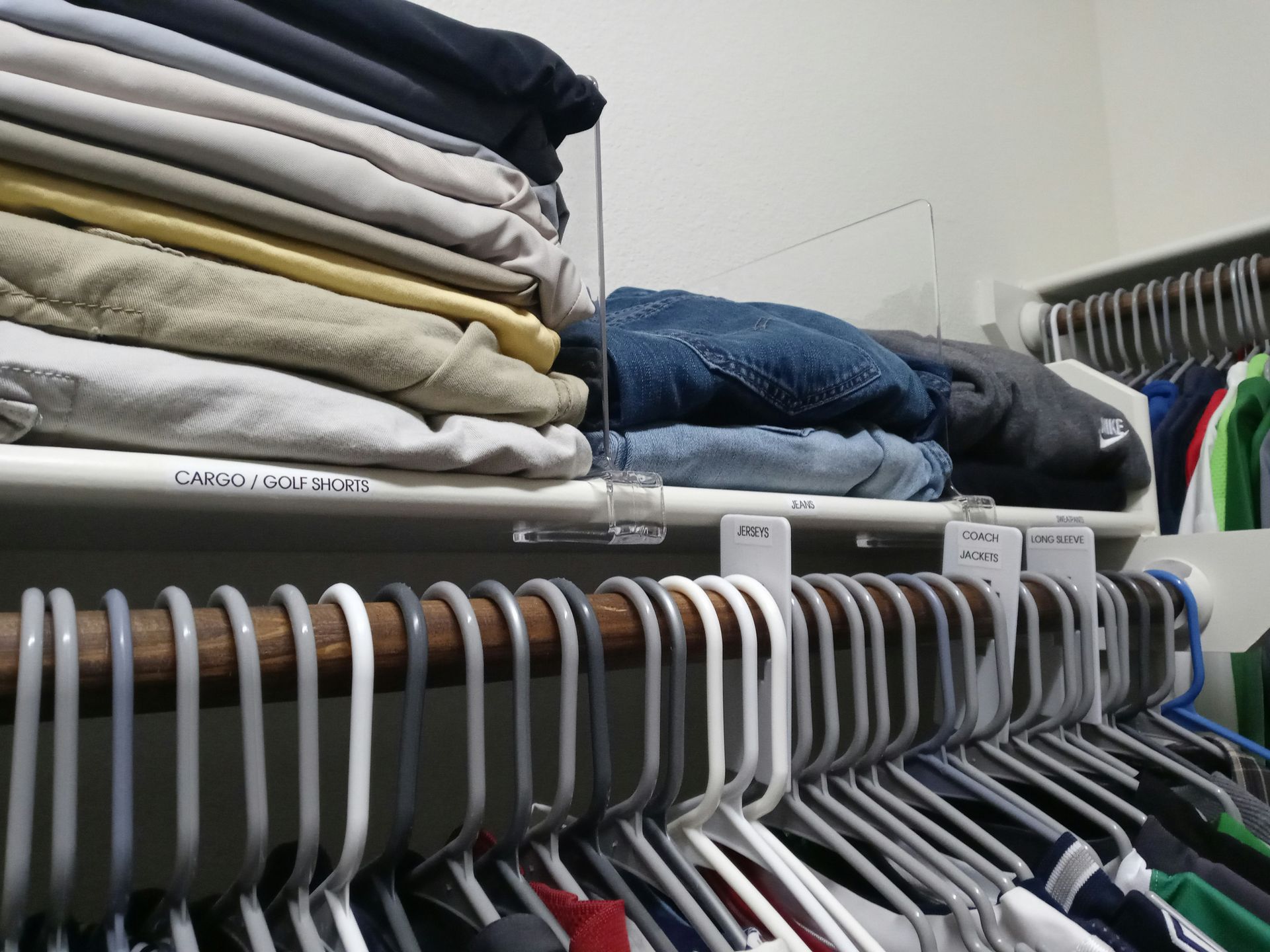 Stacks of folded clothing on a closet shelf with clear plastic dividers